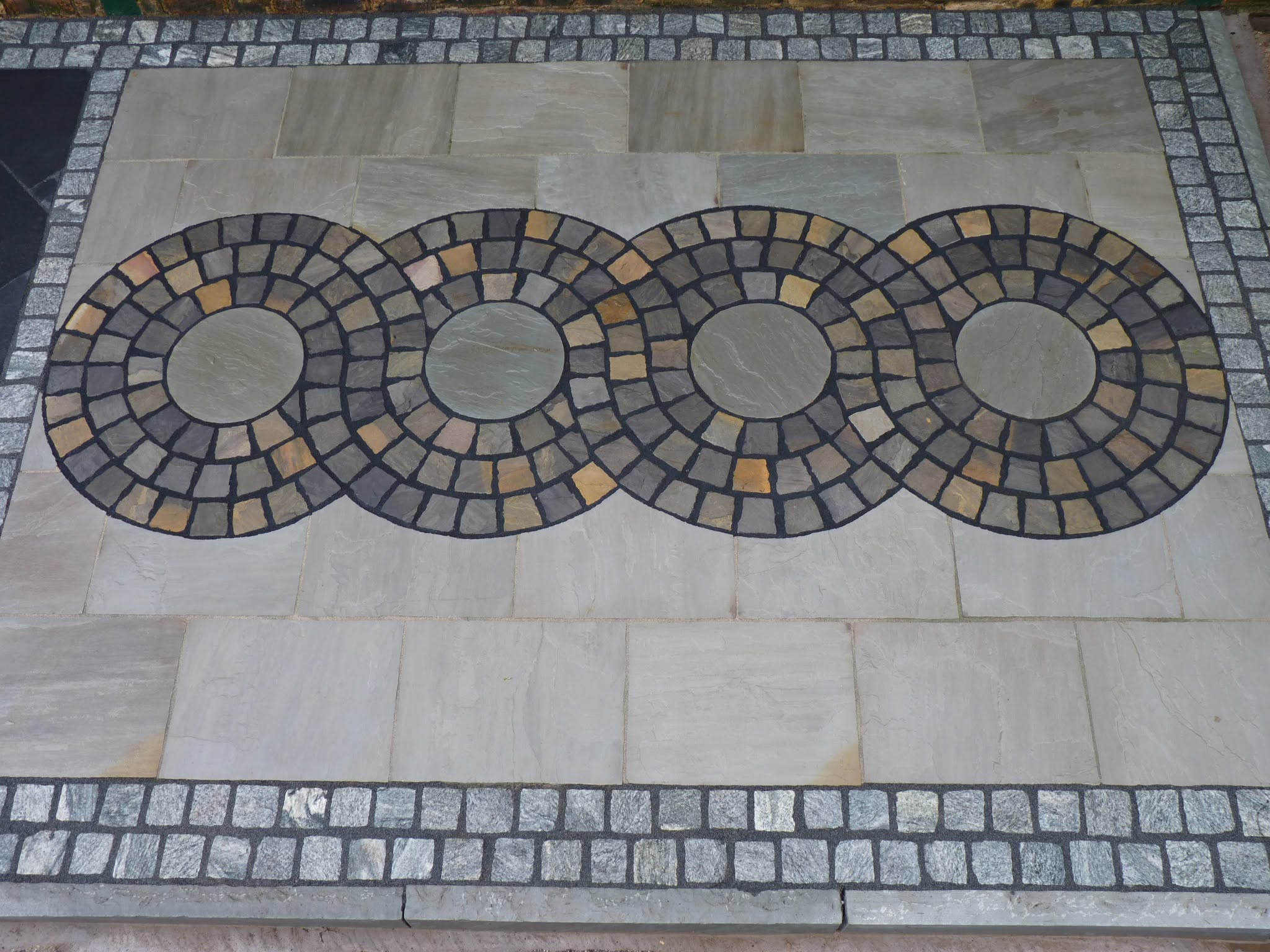 Four circle kits laid in a row in grey paving, framed by granite sett borders